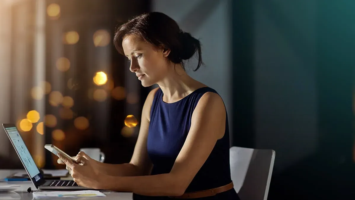Une femme sur son ordinateur et son smartphone le soir