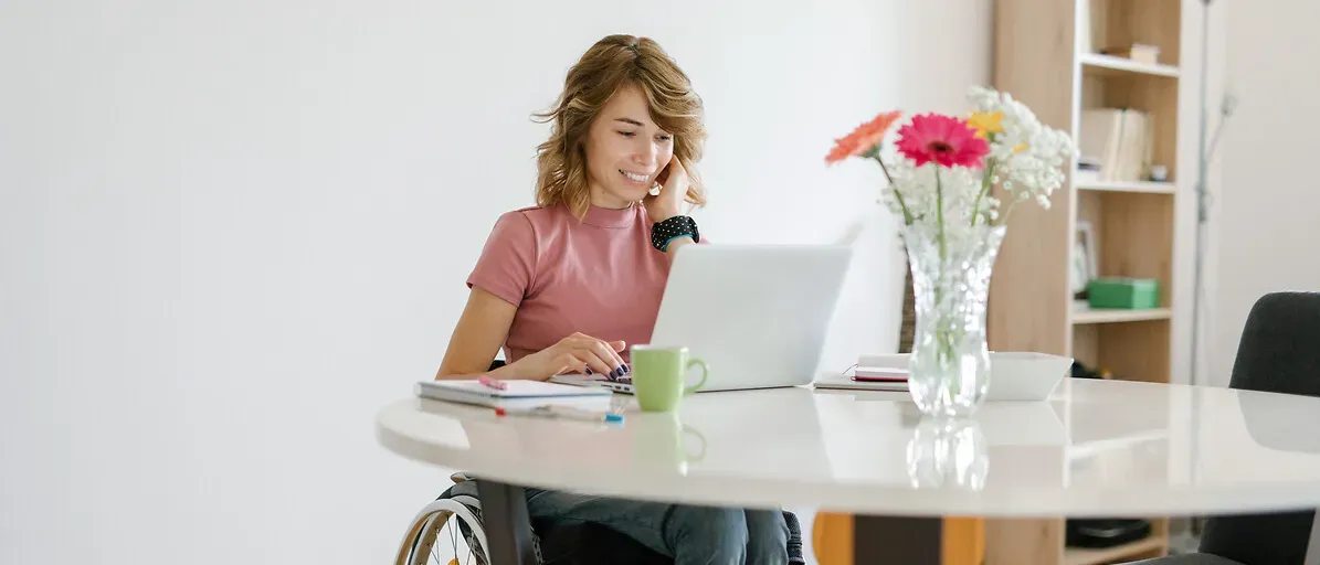 Une jeune femme en fauteuil roulant travaille depuis chez elle sur son ordinateur portable.