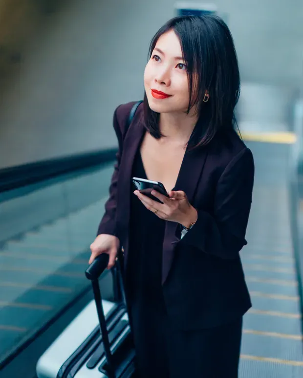 Une femme avec une valise sur un escalator consulte son smartphone