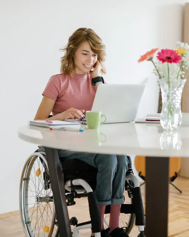  Jeune femme en fauteuil roulant travaillant à domicile sur son ordinateur portable.