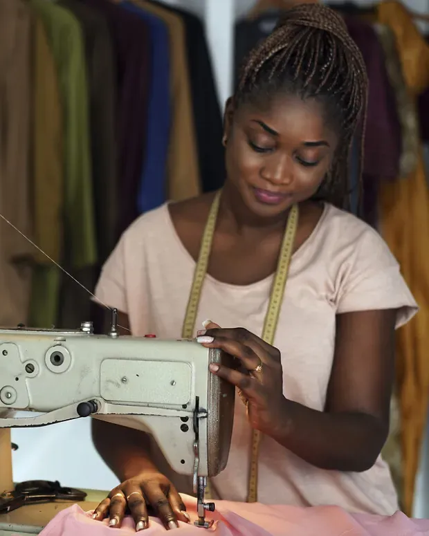 Une femme africaine coud un tissu rose à la machine, dans son atelier de couture.