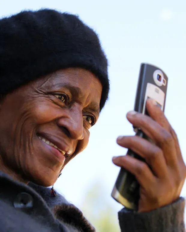 Une femme âgée souriante regarde son téléphone à l'extérieur