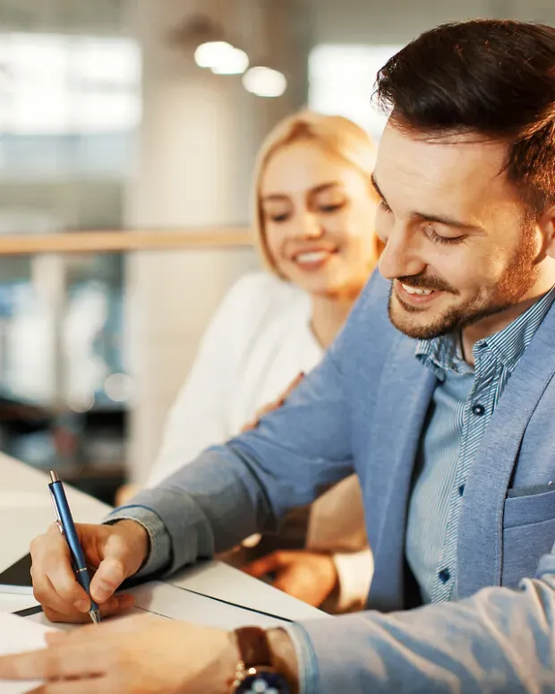 Un homme signe un document avec une femme en fond