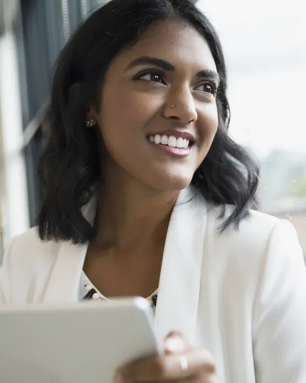 Jeune femme souriante avec une tablette regardant par la fenêtre.