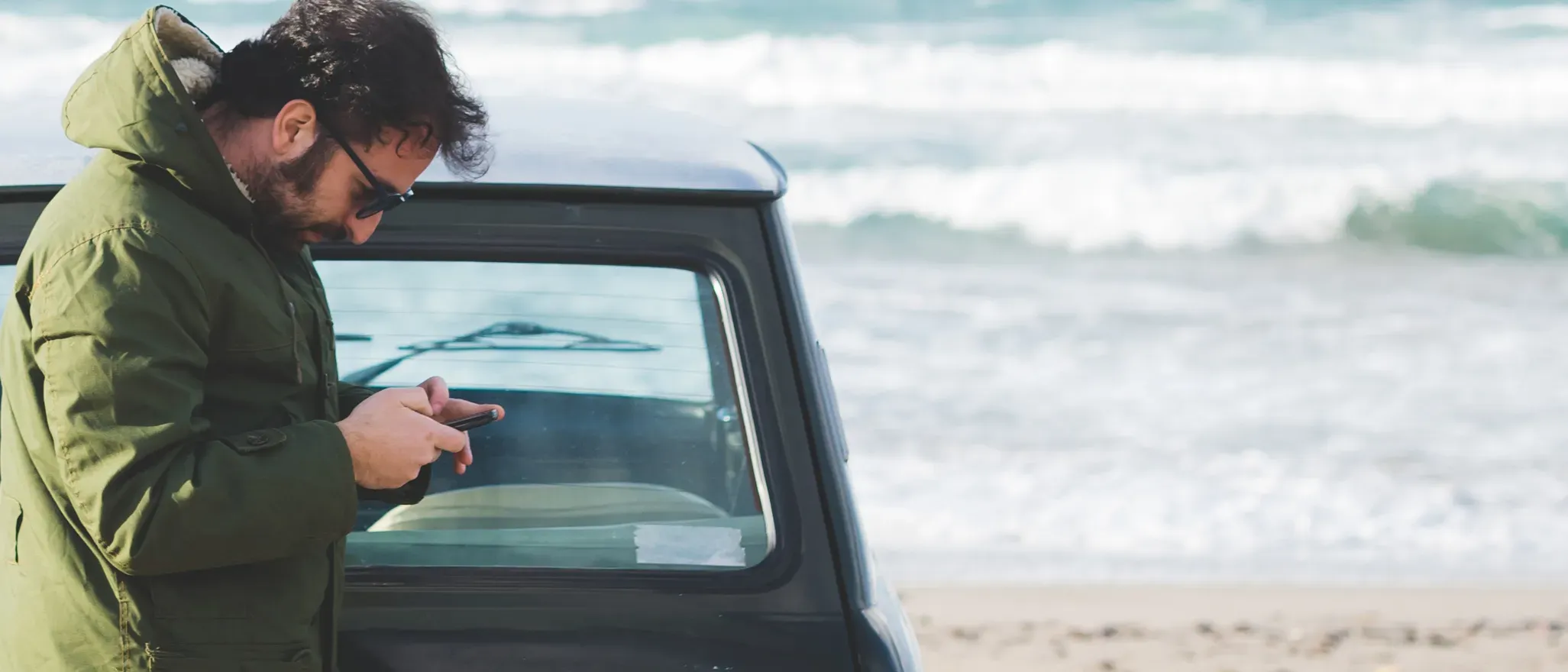 Homme consulte son mobile sur la plage devant sa voiture