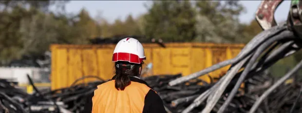 Technicienne orange devant une pelleteuse qui ramasse des cables