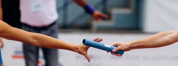 1 main féminime passe le bâton de relai dans une autre main