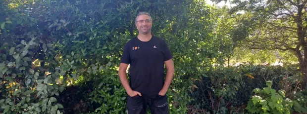 Cédric, Network Expert, smiling in front of a bush 
